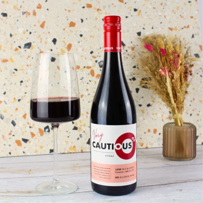 Bottle of 'Cautious' non-alcoholic red wine with a glass of red liquid on a decorative background.