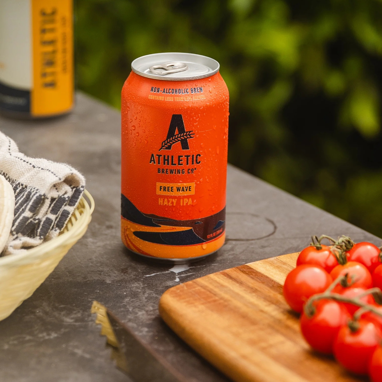 Orange can of Athletic Brewing Co. beer on a table with tomatoes and bread.
