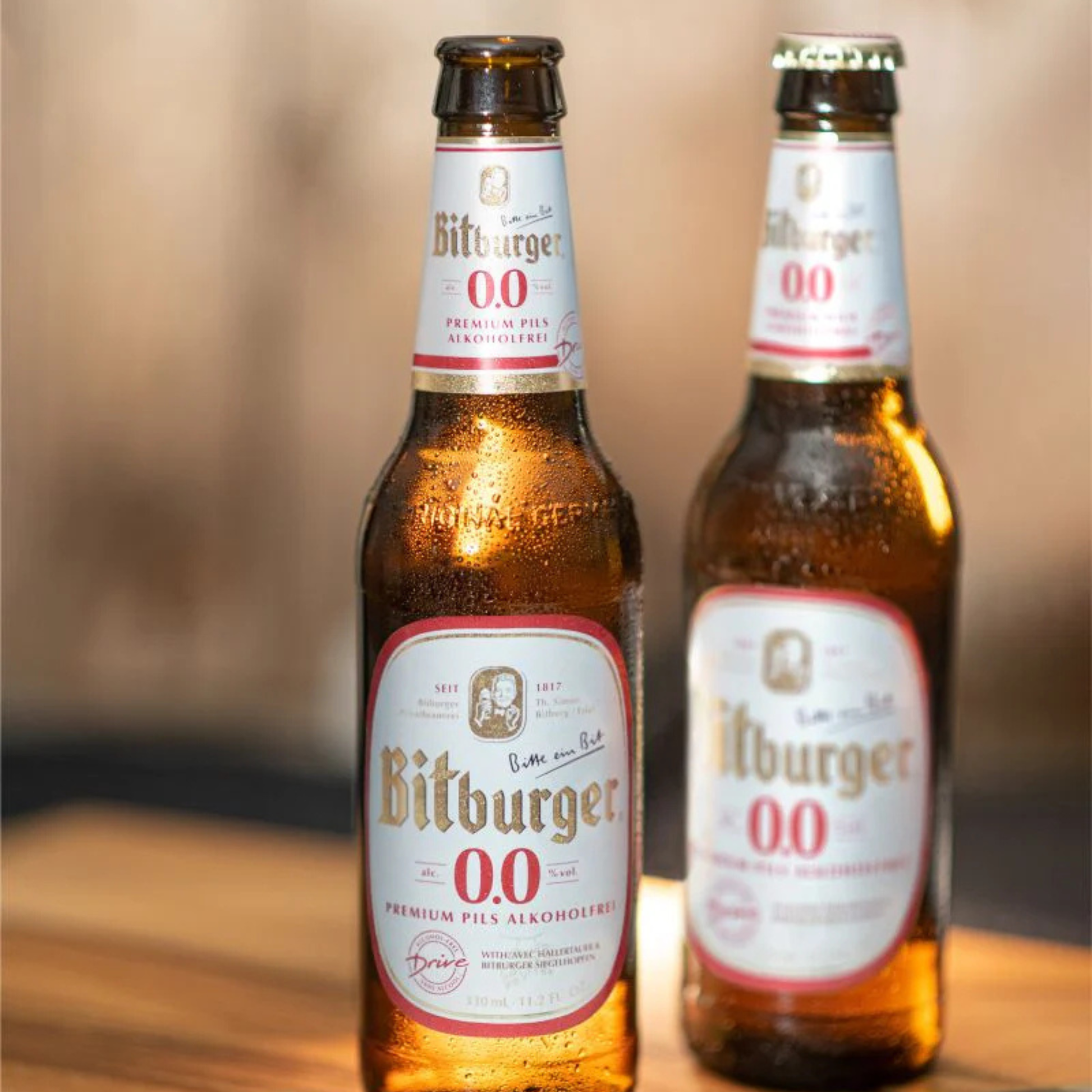Two Bitburger 0.0 bottles on a wooden surface with a blurred background