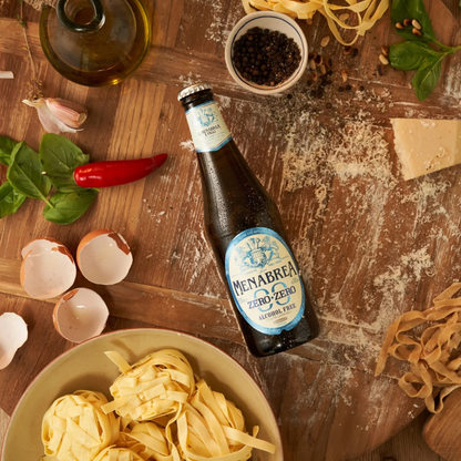 Bottle of Menabrea beer on a wooden table with pasta and ingredients