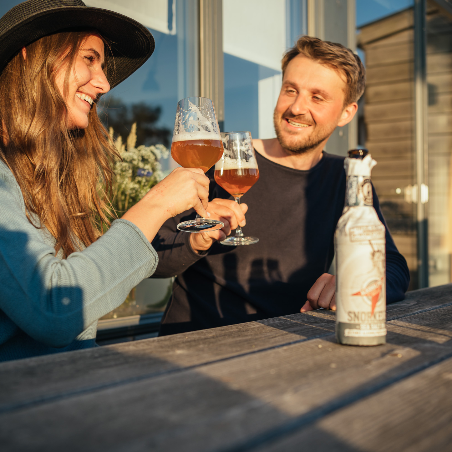 Two people enjoying drinks outdoors with a bottle of Snowy Owl on the table.