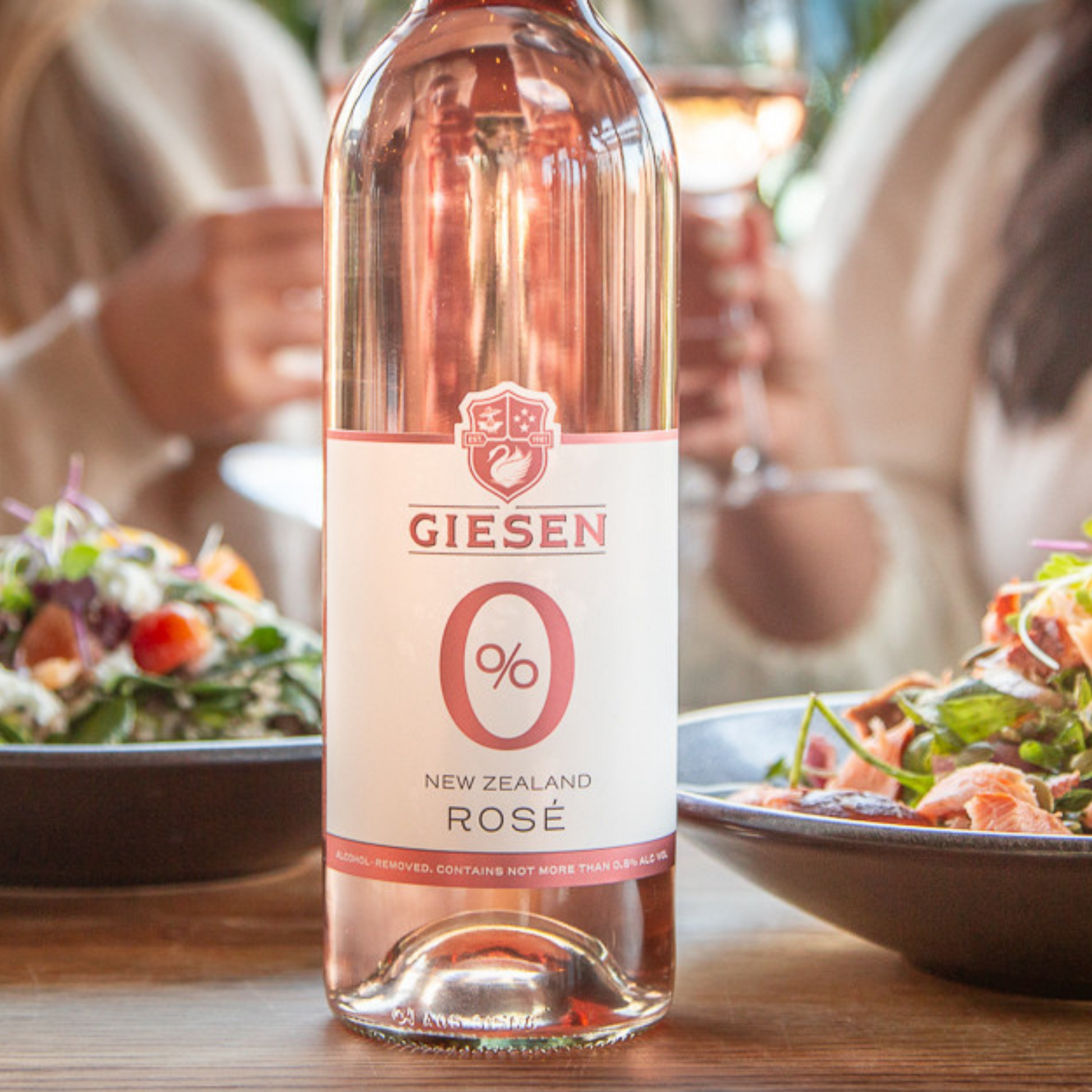 Bottle of Giesen New Zealand Rosé 0.0% wine on a table with people and food in the background