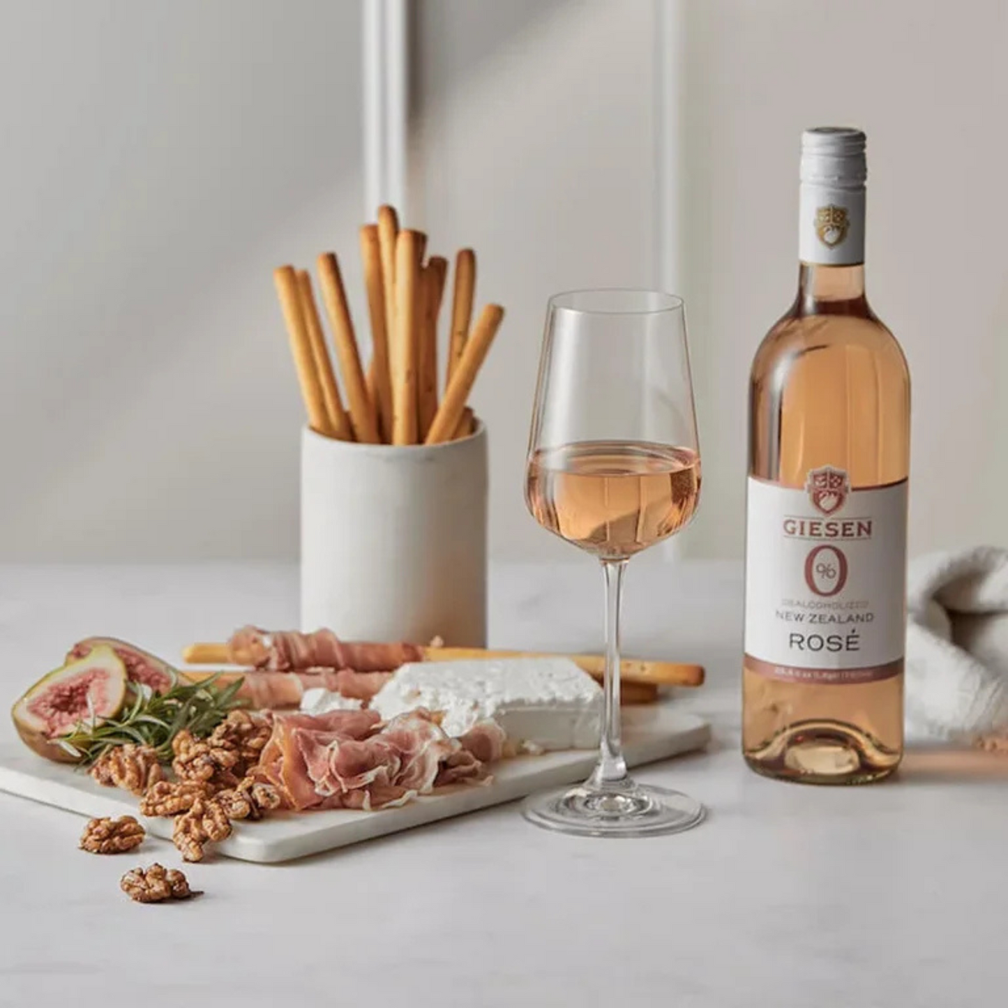 Bottle of Giesen Rosé 0.0% wine with a glass of wine and charcuterie board on a light surface.