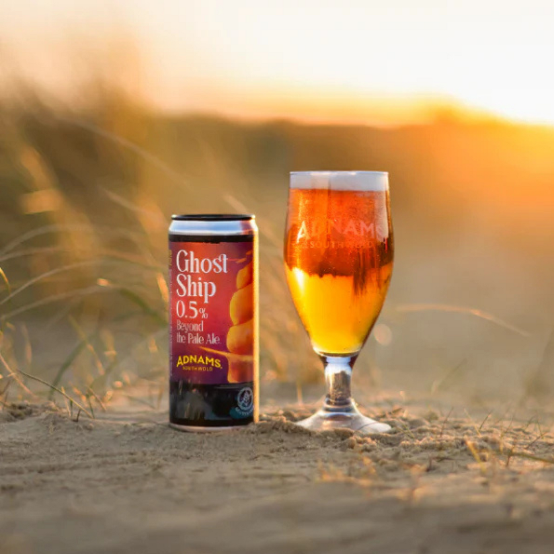 Ghost Ship beer can and glass on sand with sunset background
