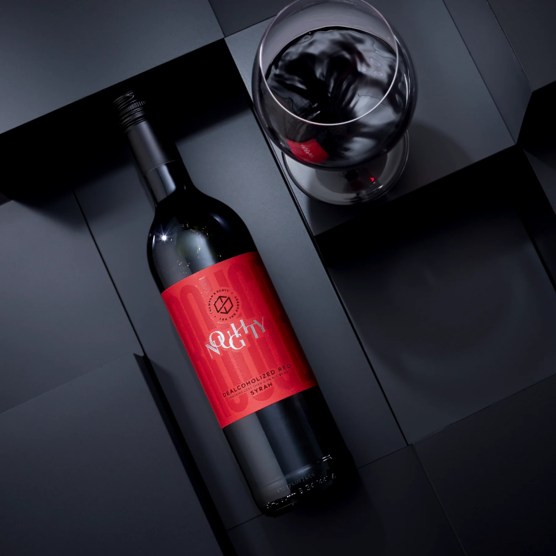 Noughty Rouge Wine bottle with red label and glass on a dark surface