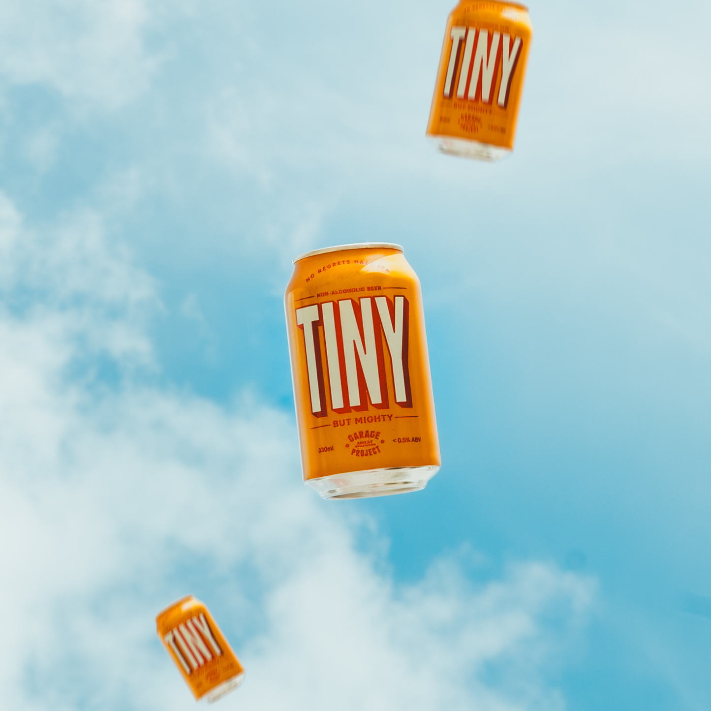 Orange 'TINY' beer cans floating against a blue sky with clouds