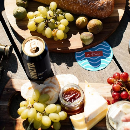 Wooden board with grapes, figs, bread, and a can of UnLTD on a table.